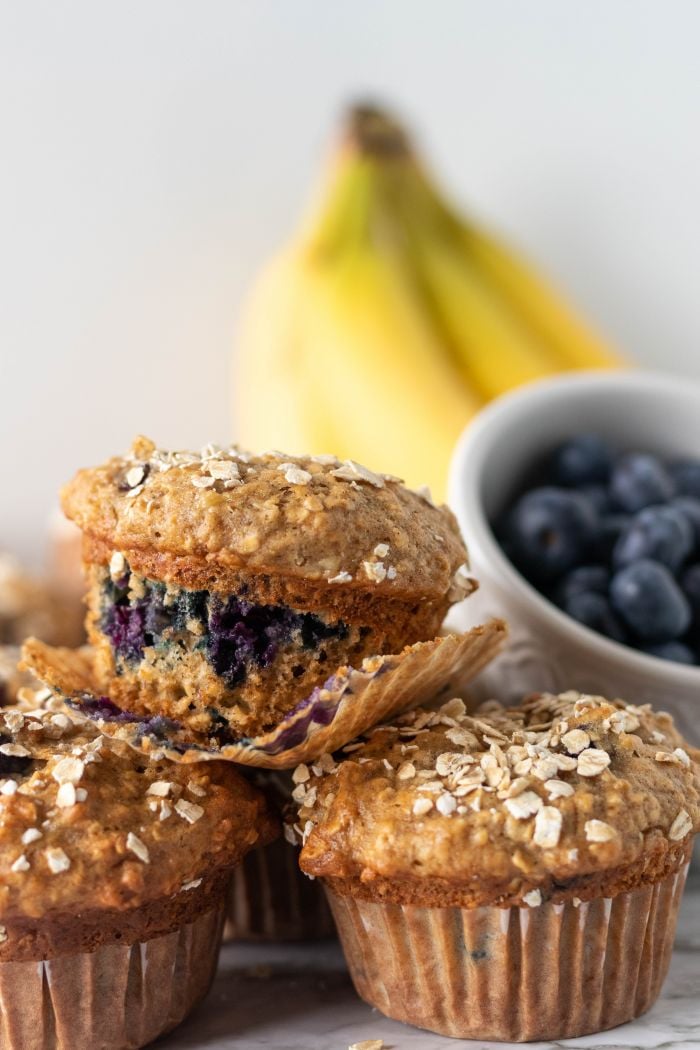 Muffin liner is partly peeled away to show the juicy blueberries in banana blueberry oatmeal muffins